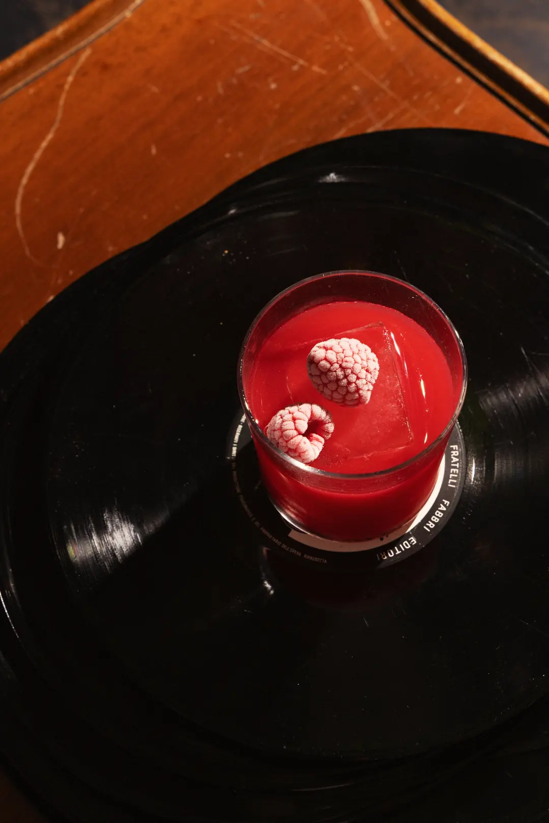 Cocktail rosso con lamponi appoggiato su un vinile