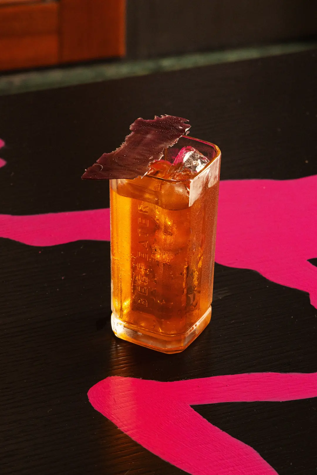 Un drink arancione con la scorza, sul tavolo nero e fucsia